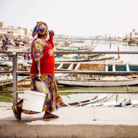 Paikallinen-nainen-ja-kalastajaveneita-Saint-Louis-Senegal-Olympia